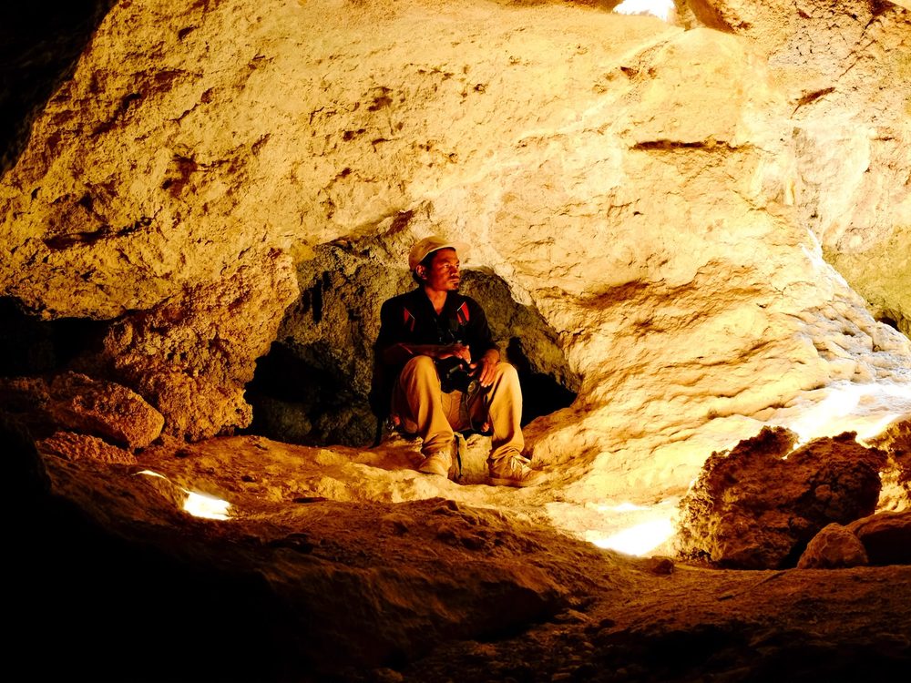 A local guide sitting inside a sunlit limestone cave