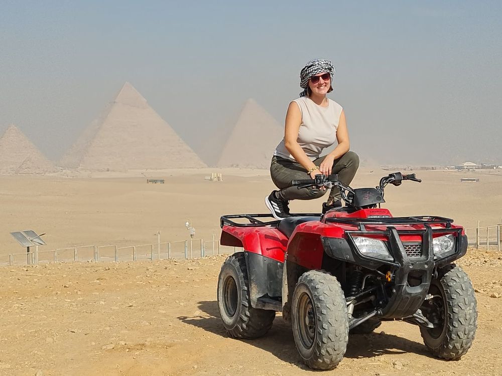 A traveller on a quad bike in the desert with the pyramids of Giza behind