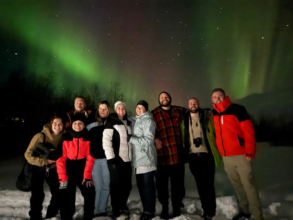 The group lined up in the snow under a green aurora in Norway