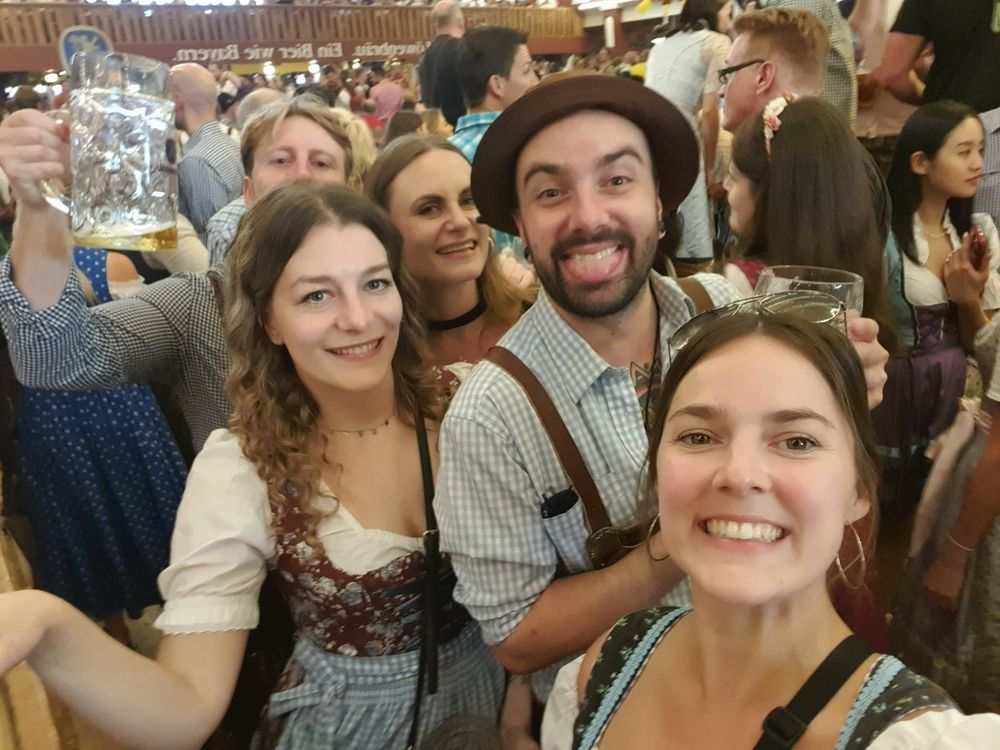 Travellers in dirndl and lederhosen raising beer steins at Oktoberfest