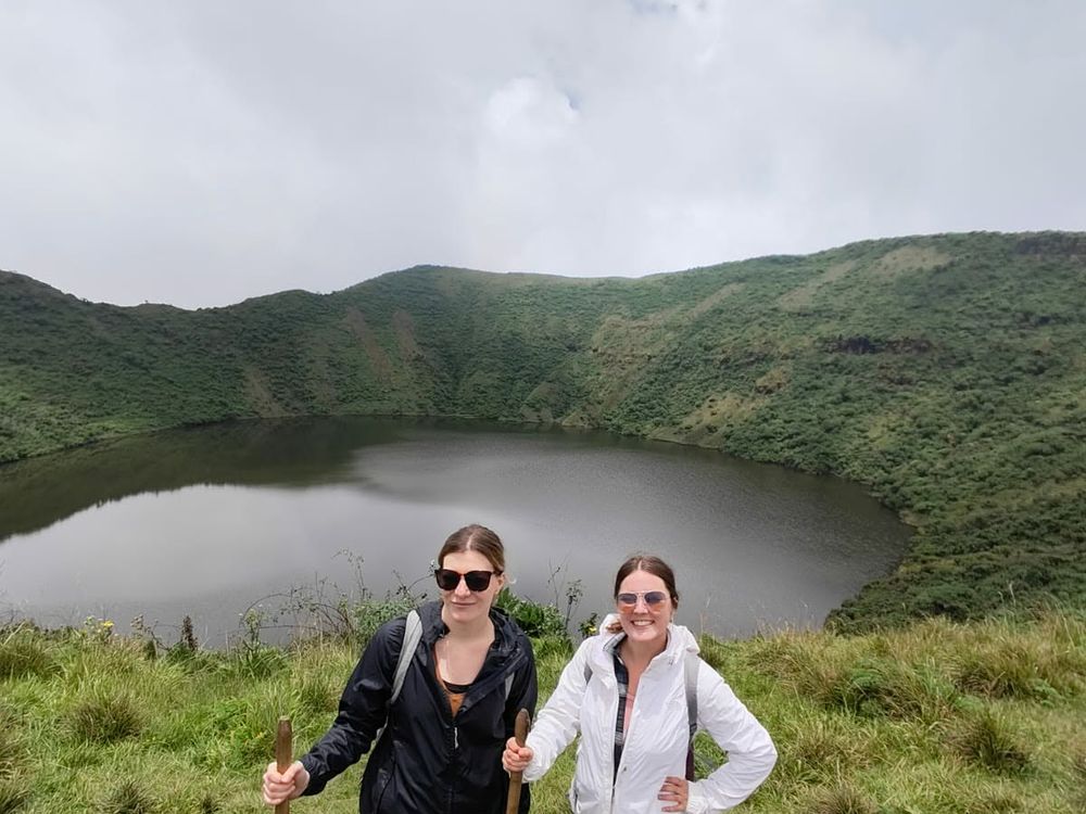 Two travellers walking above a green crater lake in the Rwandan hills