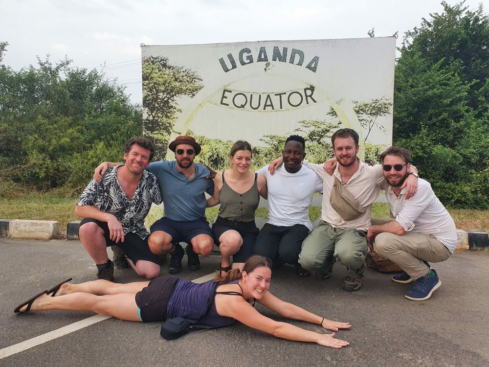 The group larking about under a painted sign marking the equator in Uganda