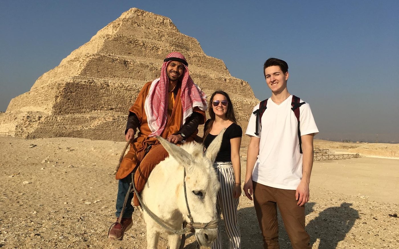 Two travellers and a local guide on a donkey in front of the Step Pyramid at Saqqara